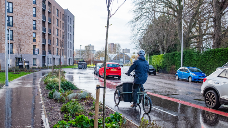 A cargo bike cyclist on a segregated cycle lane; passing new houses 
