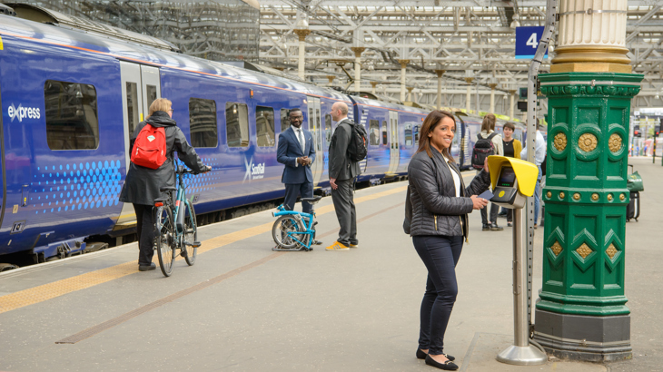 Various people use sustainable transport in Waverley Station Edinburgh. Including walking, a cyclist and in the foreground a commuter buys a ticket.
