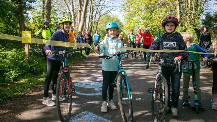 Wylam Waggonway launch event - Image of children with bikes cutting ribbon - spring day - sunny in a crowd under trees