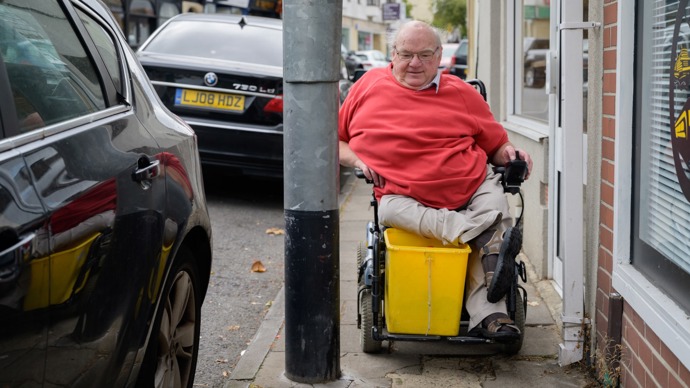 A man using a wheelchair navigating along a narrow pavement in Bristol