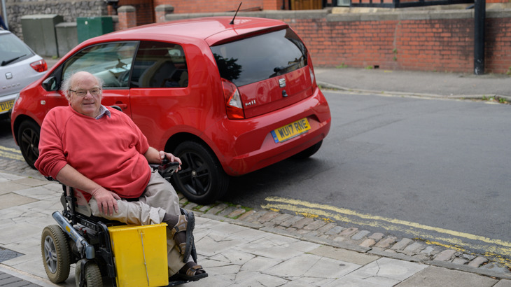 A man using a wheelchair smiling on a residential street in Bristol