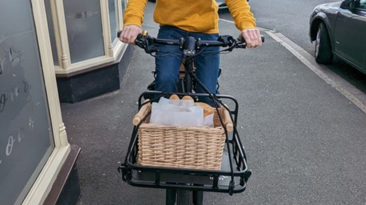 Close up of bread in the black metal front basket of an e-cargo bike. Hands can be seen on the handlebars above.
