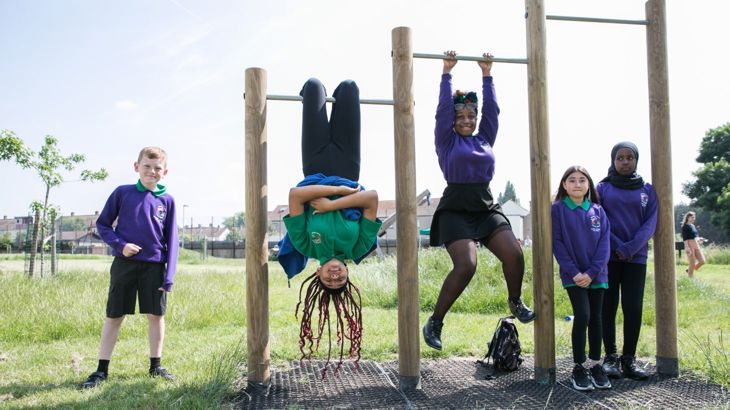 Children playing on a climbing frame. The frame is made of oak and steel. there are three sections to the frame. the children are hanging upside down and the mood is cheerful. Behind them there is mown grass.