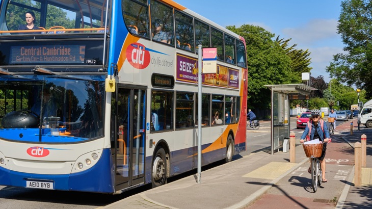 A woman on a bicycle cycles alongside a bus stop on a segregated cycle lane in the summer