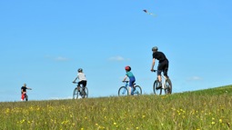 A family cycling over the ridge of a hill in the Chilterns, with another playing with a kite against a clear blue sky