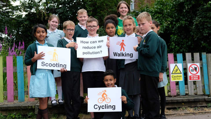 School children holding up a sign that says "How can we reduce air pollution?"