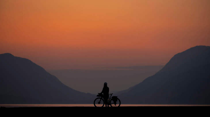 Orange sunset with a silhouette of a person standing with a bicycle