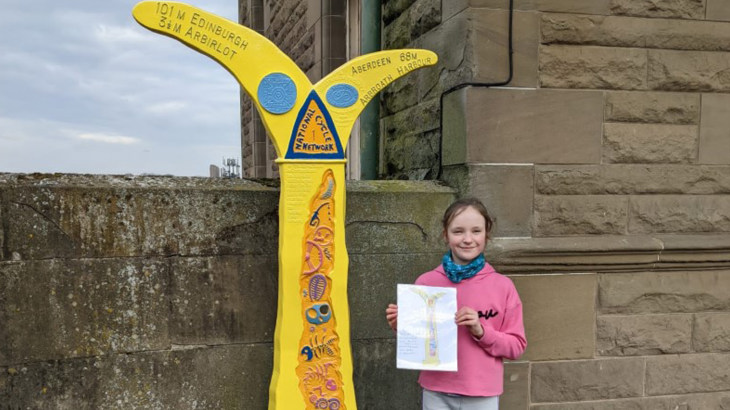 Aoife, the winner of the Girlguiding Scotland Milepost competition, stands beside her winning design painted on a Millennium Milepost outside Arbroath Rail Station