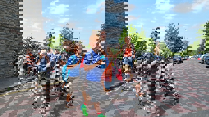 Children walking across a road while a woman pushes a buggy in the background