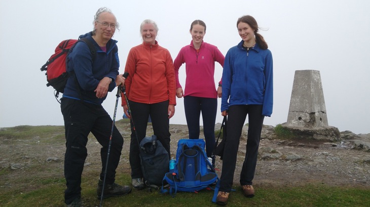 The Prince Family smiling and standing together at the top of a mountain in the Scottish Highlands