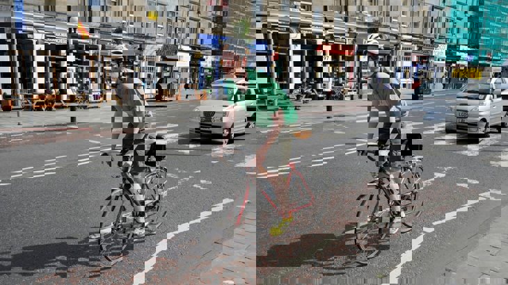 Man cycling on road with car in background