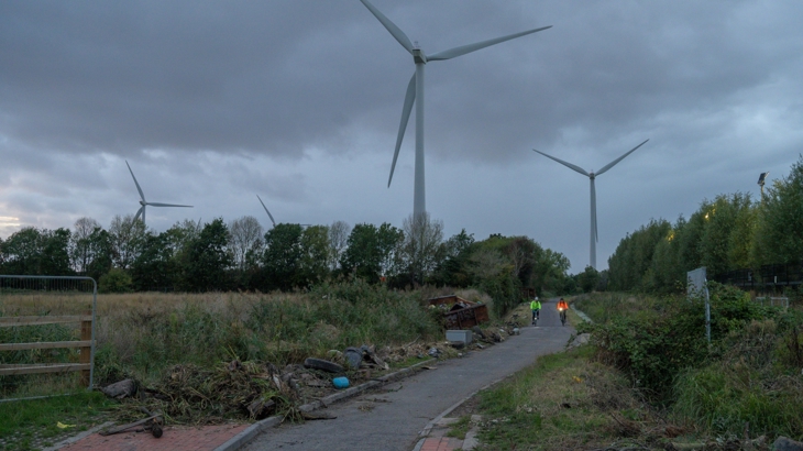 unlit walking and cycling route, two cyclists with hivis and lights on using it before construction work begins to install lighting. 
