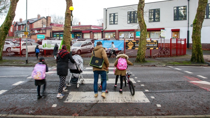A family crossing the road at a zebra crossing wheeling a buggy and bikes