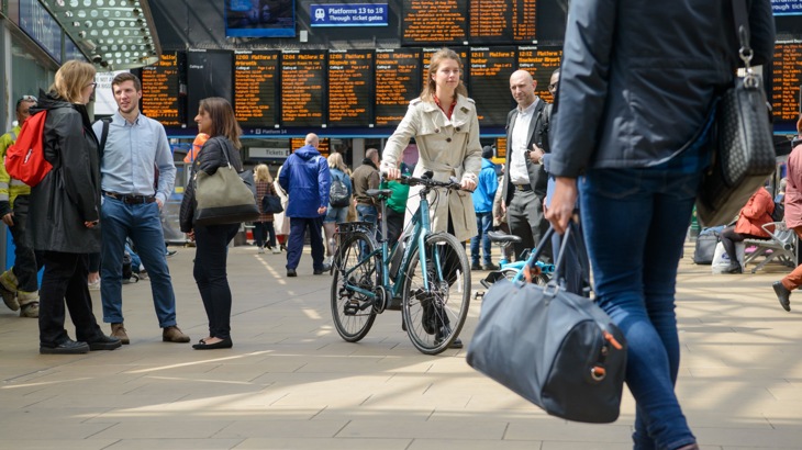 People walking and wheeling bikes through a busy train station
