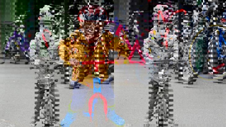 Toddler with helmet and yellow coat on, riding a red bicycle