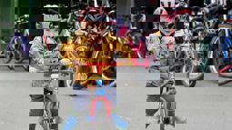 Toddler with helmet and yellow coat on, riding a red bicycle