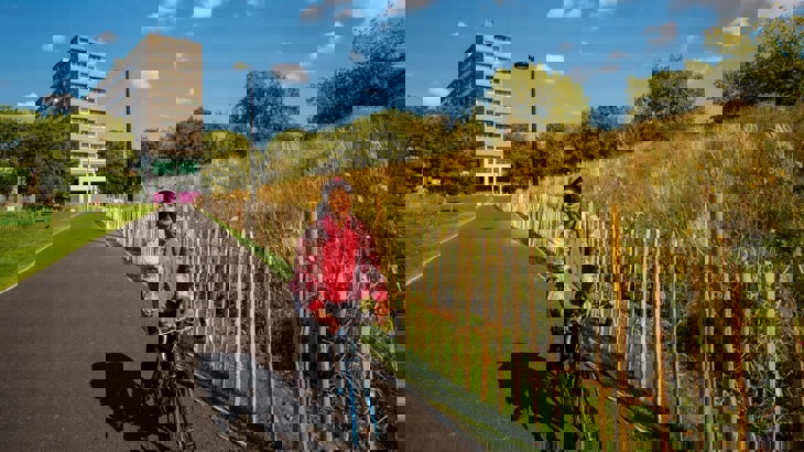 A young female cycles along a traffic-free path with a tower block in the background 