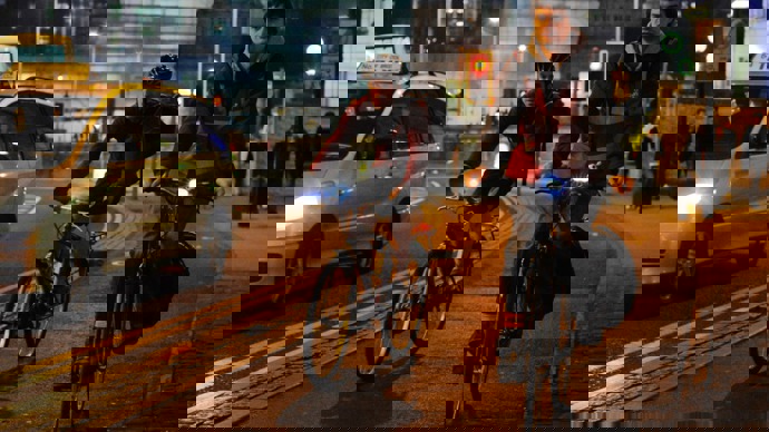 Two men cycling in the dark in a busy city landscape