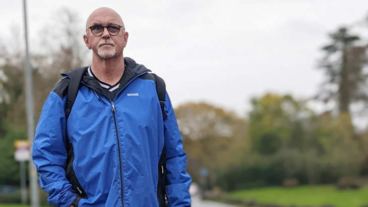Mark, wearing a waterproof jacket, walking in a local park surrounded by grass and trees