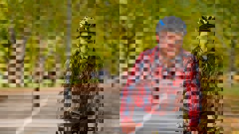 Man in red shirt and cycling helmet riding on cycle path through wooded park