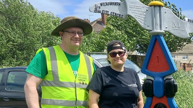Sara and Vince, Walk Wheel Cycle Trust volunteers standing next to a millenium milepost. 