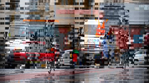 A man cycles in the rain in a city while wearing a high vis vest