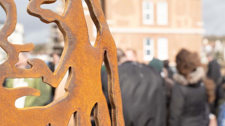 portrait statue at unveiling event in Hastings. People gather for event behind the statue.