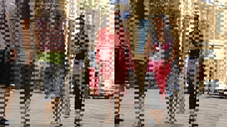 Two female friends walking through high street with others walking in the background