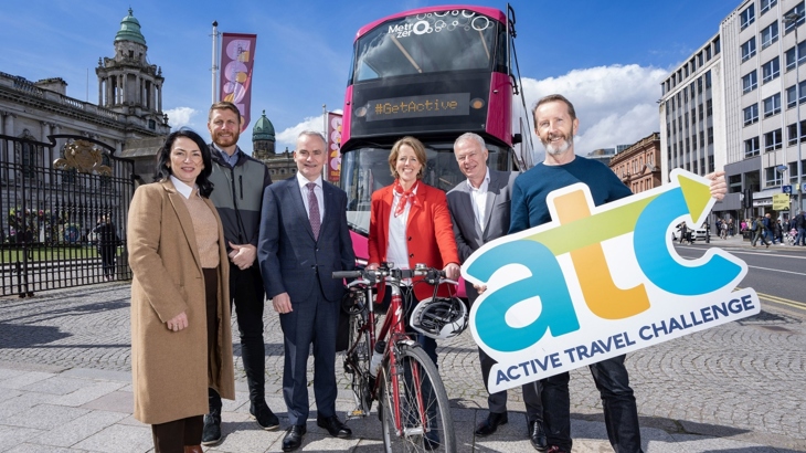 A group of women and men stand with a bicycle in front of a bus with a sign reading 'ATC' to launch the active travel event which happens in June.