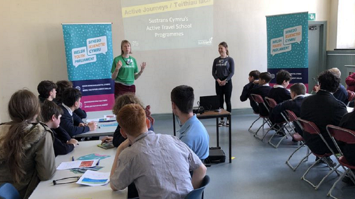 Two Walk Wheel Cycle Trust colleagues presenting to audience of pupils in Blaenau Ffestiniog