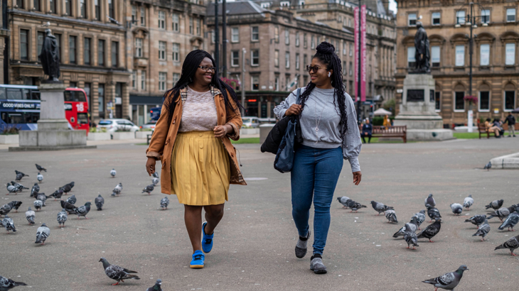 Two women walking and smiling at each other while walking in the centre of Glasgow