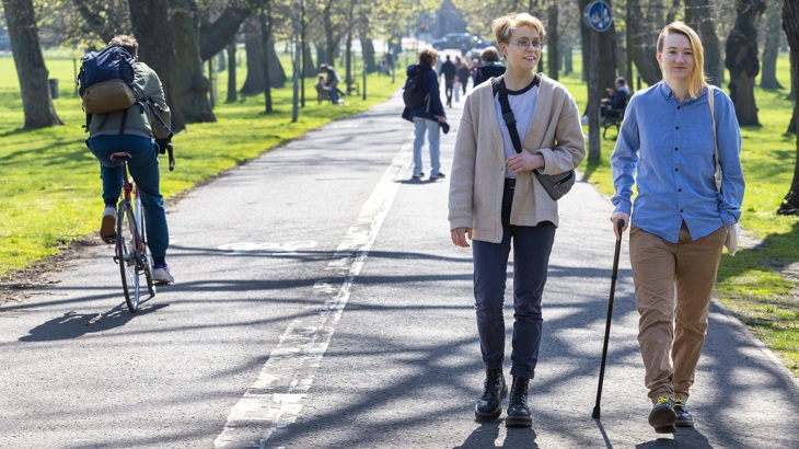 Two people are shown walking forwards on a shared use path. They are being passed by a cyclist going the other way on the other side of the path.