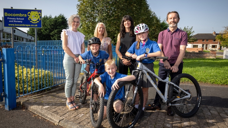 Children and staff from Bocombra Primary School join representatives from Walk Wheel Cycle Trust and the funders PHA and DfI outside the school on a sunny day.