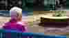 Elderly woman sitting on a bench surrounded by artworks and planters in Leith.