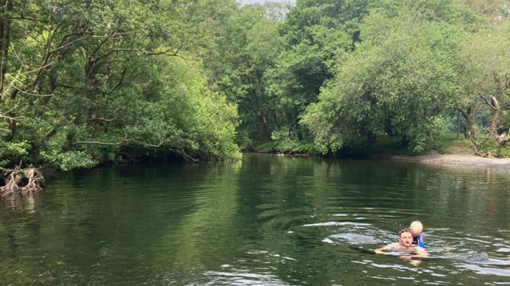 A man and a boy swimming in a river surrounded by greenery