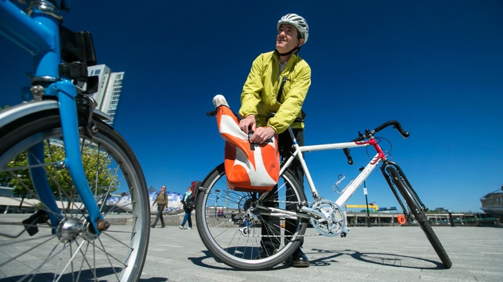 A man wearing a helmet and high-vis yellow jacket is closing up a bag attached to his bike.