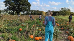 Woman and family standing in pumpkin patch field with blue skies.