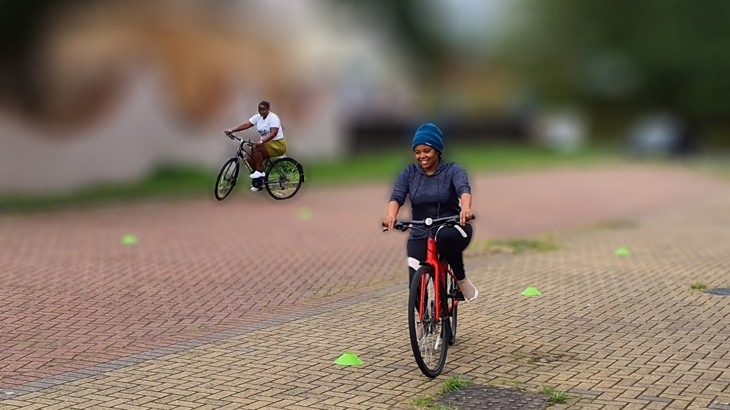 Two women smiling while cycling through cones on their two-wheeled bicycles