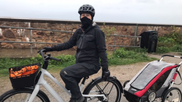Image of Nia on her e-bike with a trailer attached, wearing waterproof gear.