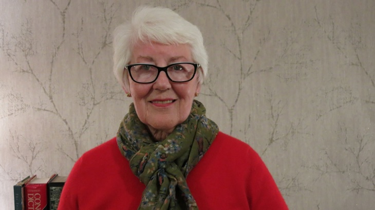 Fay Anderson is pictured at home wearing a red top and floral scarf.
