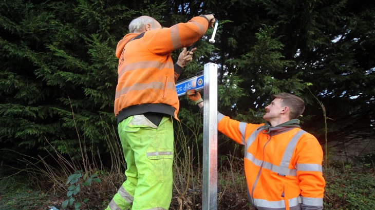 two men install a sign on a walking and cycling route