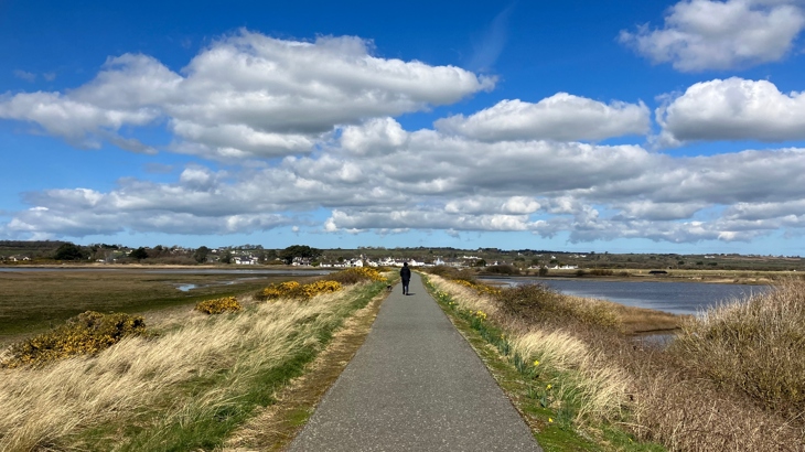 A walker on an NCN route in Wales, with an estuary either side of the path.
