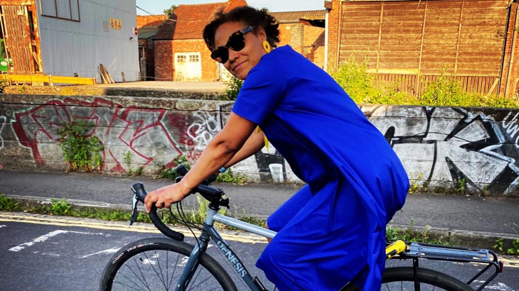 A woman in a blue dress and black sunglasses on cycling in an urban area