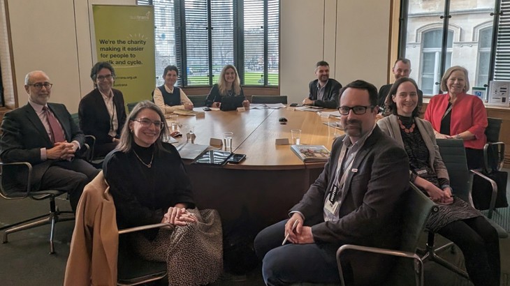 A group of men and women, members of Parliament and representatives of Walk Wheel Cycle Trust and other organisations, sit in work attire around a table.