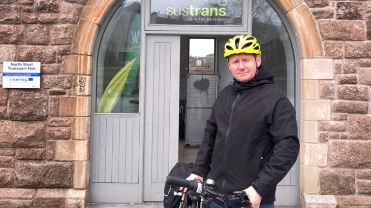 A man wearing a yellow helmet stands with a bicycle outside our Active Travel Centre in Derry.