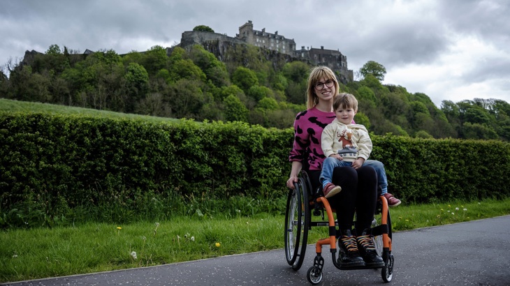 A parent and child are shown using a wheelchair with Stirling Castle in the background.