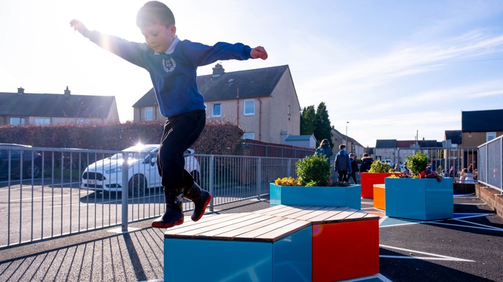 A school pupil is shown jumping on a piece of outdoor equipment in the grounds of their primary school.