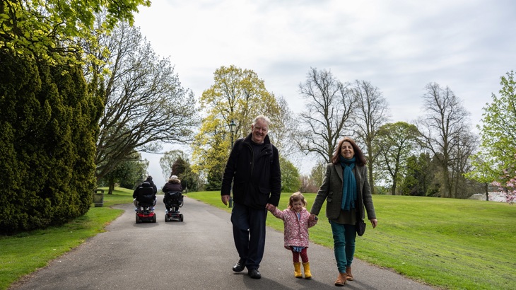 Two adults are shown walking with a young child through a park.