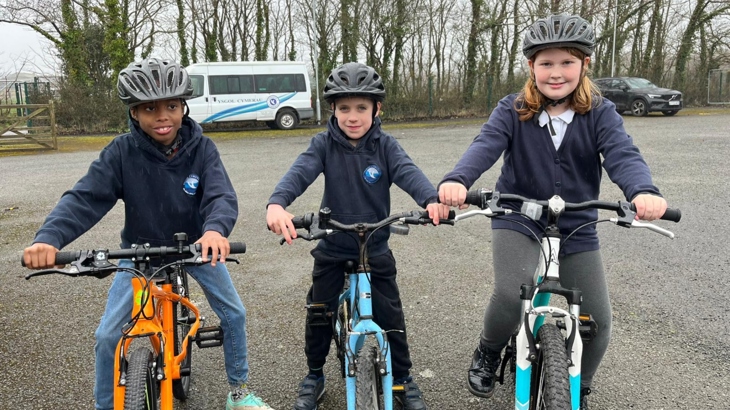 Pupils from Ysgol Cymerau posing for a photograph on their school yard on their bikes, wearing helmets.