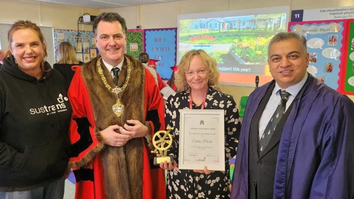 A woman holds a certificate and a trophy with a man in ceremonial robes on each side of her and a female Walk Wheel Cycle Trust active travel officer on the left.